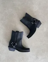 Botas de cuero negras, de caña media, con punta cuadrada, tira ancha con hebilla metálica y taco de madera.