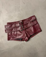 Shorts de efecto cuero color bordó con tiro alto y múltiples correas ajustables con hebillas y ojales metálicos plateados.