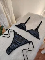 Conjunto de bikini negro de cuerina, con corpiño triangular y bombacha colaless con tiras laterales ajustables.
