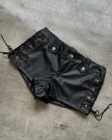 Short de cuero sintético negro, tiro alto, con trabillas y presillas con botones plateados. Presenta cordones cruzados en los laterales.