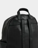 Mochila urbana negra de cuerina con bolsillo frontal con cierre y charm colgante de cadena con dije de corazón y candado. Tiene correas regulables, manija superior, cierre superior, doble bolsillo frontal (uno con charm metálico) y bolsillos laterales.