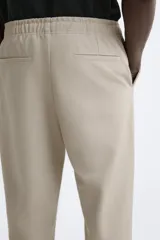Pantalón de jogging color beige confeccionado en tejido de mezcla de algodón. Cuenta con cintura elástica ajustable con cordón, bolsillos frontales y traseros.