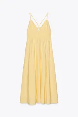 Vestido midi amarillo de tejido fluido con escote pico y tirantes finos cruzados en la espalda ajustables con lazada. Tiene detalle de elásticos bajo el pecho.