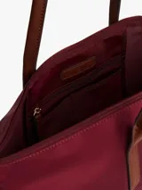 Cartera tote de nailon color borgoña, con forma flexible y asas superiores de cuero marrón. Presenta un cierre de cremallera, bolsillo interior con cremallera y dos bolsillos abiertos interiores. En el frente lleva una insignia metálica dorada con el monograma TH.