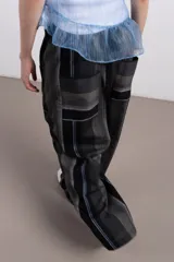 Pantalón de corte amplio confeccionado en tejido seersucker con textura rayada en tonos grises, negros y celestes. Presenta bolsillos laterales con apliques rectangulares en contraste y cintura elástica con cordón ajustable.