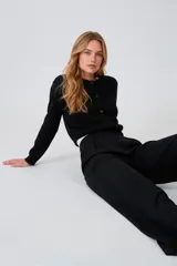 Cardigan negro de acrílico, ajustado al cuerpo, con cuello a la base, manga larga y cierre frontal con botones.