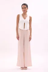 Pantalón de tela color rosa pálido, de corte palazzo y cintura alta con elástico. Presenta aberturas circulares verticales en los laterales.