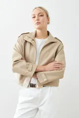 Chaqueta corta color beige de cuero sintético, con cuello alto, cierre frontal con botones a presión y bolsillos laterales con solapa.