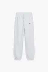 Pantalón de jogging gris claro, de tiro alto, con cintura elástica ajustable con cordones, bolsillos laterales y texto estampado en el frente.