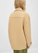 Abrigo corto color beige, de corte recto y doble botonadura. Tiene cuello con solapa, bolsillos laterales y mangas largas con puños abotonados.