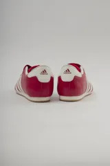 Championes Adidas rojos de cuero sintético, diseñados para taekwondo. Presentan el logo de Adidas en la lengüeta y las tres rayas blancas características en los laterales. El interior es acolchado y de color blanco.