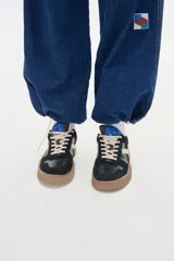 Zapatillas deportivas negras con detalles en blanco y suela color caramelo.