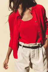 Chaqueta roja de punto con cuello redondo y manga larga. Tiene bolsillos delanteros de plastrón, cierre frontal con botones dorados con relieve y acabados en rib.