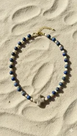 Collar corto con cuentas de piedra natural lapislázuli mate y cristales facetados beige, con dije de cruz de piedra natural y cadena dorada ajustable.