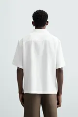 Camisa color marrón oscuro de corte relaxed fit, confeccionada en tejido de lino. Tiene cuello bowling, manga corta, bajo con aberturas laterales y cierre frontal de botonadura.