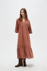 Vestido largo color marrón, con escote en V, mangas 3/4 y detalles de broderie en el pecho, mangas y falda. La falda tiene un volado en el ruedo.