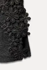 Top de punto canalé color gris oscuro, de cuello alto y sin mangas. Presenta apliques de encaje floral en los laterales del ruedo.