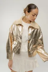 Campera corta dorada de cuero sintético metalizado con cuello de piel sintética color crema, cierre frontal con botones marrones y bolsillos de parche en el pecho.