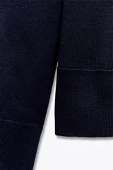 Jersey de punto color verde oliva, con cuello redondo y manga larga. Tiene bajo con aberturas laterales y acabados en rib.