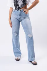 Jeans de mezclilla azul claro, tiro alto, corte wide leg y roturas a la altura de las rodillas.