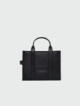 Bolso tote de cuero negro Marc Jacobs, tamaño mediano, con doble asa corta y correa larga extraíble. Estampado frontal con el texto "THE TOTE BAG" y el nombre de la marca.