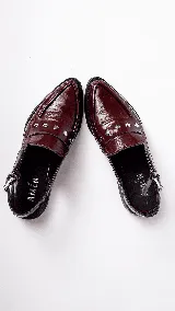 Mocasines color borgoña de cuero con punta fina, detalle de apliques metálicos y tira trasera con hebilla.