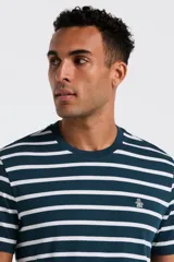 Remera de manga corta, cuello redondo, color verde azulado oscuro con rayas horizontales blancas. Presenta un pequeño logo bordado en el pecho.