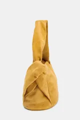 Bolso de mano color mostaza, de serraje, con asa ancha con detalles y cierre mediante hebilla metálica.