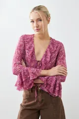 Blusa fucsia estampada con volados, escote en V y mangas largas acampanadas.
