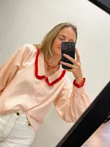 Camisa de algodón a rayas verticales color rosa y blanco, con cuello babero y puños con volantes rojos.