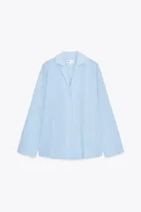 Camisa oversize celeste con textura de algodón, cuello solapa y manga larga. Presenta pliegues delanteros y bajo asimétrico.