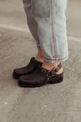 Zuecos de cuero marrón oscuro con hebilla lateral ajustable y base robusta. Diseño cerrado adelante con taco medio.