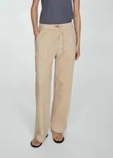 Pantalón color beige de tiro medio, corte recto y diseño largo. Cuenta con dos bolsillos delanteros, cierre de lazo y dos bolsillos de parche en la parte posterior.