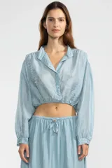 Blusa corta celeste en tejido arrugado liviano, con cuello mao, botones al frente, mangas abullonadas y ruedo elastizado.