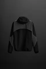 Cazadora con capucha confeccionada en tejido técnico ligero y elástico en todas las direcciones, color negro con detalles en gris. Cuenta con cuello con capucha ajustable, manga larga, bolsillos con cierre de cremallera en cadera, acabados con elástico y cierre frontal de cremallera.