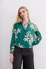 Camisa verde esmeralda con estampado de hojas color crema, escote redondo con lazo ajustable, mangas largas con puños elastizados y volados.