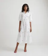 Vestido camisero midi blanco con estampado de flores rosas y celestes, manga corta abullonada, cuello camisero, abotonado al frente y falda con volantes.