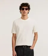 Remera de mangas cortas color crema, confeccionada con 50% algodón y 50% poliéster, con cuello redondo y tejido texturizado.