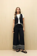 Pantalón negro de corte palazzo con bordado geométrico en el ruedo.