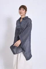 Camisa blanca de lino con cuello clásico, cierre frontal con botones, mangas anchas 3/4 y detalles de bordado calado en el canesú y los puños.