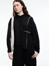 Camisa de manga larga de lino color azul con calce relajado y diseño asimétrico. El bolsillo delantero está colocado de forma invertida, un detalle lúdico que rompe con lo clásico. Lleva un bordado tipo pespunte en color contraste que recorre el frente y el bolsillo.