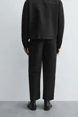 Pantalón negro relaxed fit confeccionado en tejido con algodón, lino y lyocell. Cintura con detalle de pliegues frontales dobles, bolsillos delanteros y traseros. Cierre frontal con cremallera y botón.