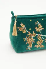 Bolso de mano tipo clutch, color verde esmeralda, de terciopelo con bordado de flores amarillas y blancas. Incluye un cierre superior y un colgante de borla dorada.