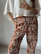 Pantalón de tela color terracota con estampado de hojas y flores en color blanco.