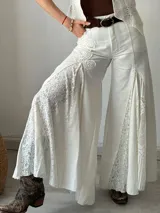 Pantalón blanco de corte palazzo con aplicaciones de encaje floral en los laterales.
