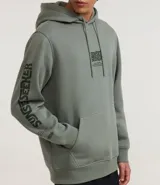 Hoodie masculino de algodón y poliéster, color verde salvia, con capucha ajustable, bolsillo canguro y estampado en el pecho y en la manga izquierda con texto.