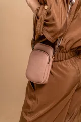 Bandolera pequeña tipo 'phone bag' de símil cuero color rosado pálido, con cierre de cremallera y correa ancha de tela con diseño de chevron en tonos claros.