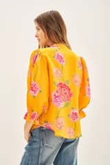 Camisa color naranja con estampado de flores rosas, escote redondo, mangas al codo terminadas con elástico y volado. Confeccionada en viscosa estampada.