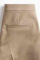 Pantalón cigarette tobillero color beige, con cintura estándar, cierre y pretina prolongada con corchete oculto. Piernas ajustadas con abertura corta en los bajos, bolsillos al bies y bolsillo de atrás decorativo. Pliegues adelante y atrás.