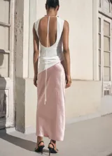 Falda midi de tiro medio, corte recto, color rosa pálido con efecto arrugado y brillo satinado. Presenta un diseño asimétrico en la parte superior, posiblemente superpuesto a un top blanco.